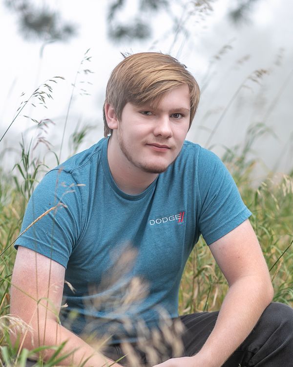 Portrait in tall grass of person wearing blue t-shirt with soft natural lighting. Senior Portrait Photographer | Denver, Broomfield, Boulder