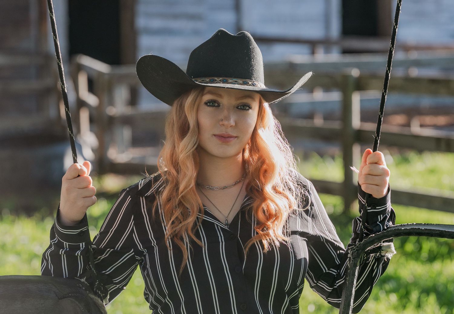 A person wearing a striped shirt and black hat swings on a rope swing while casually smiling at the camera.