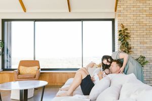 Family relaxing together on a cozy sofa in a modern living room with large windows and brick wall.