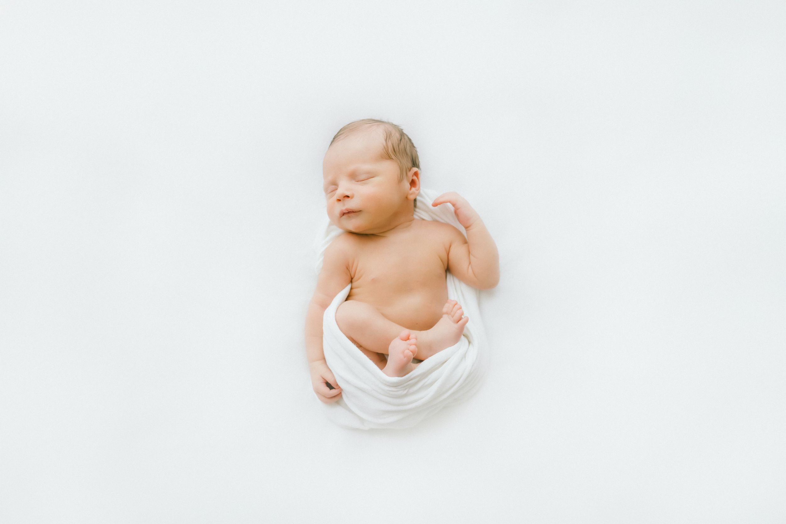 Peaceful newborn baby sleeping wrapped in a soft white swaddle on a white background.