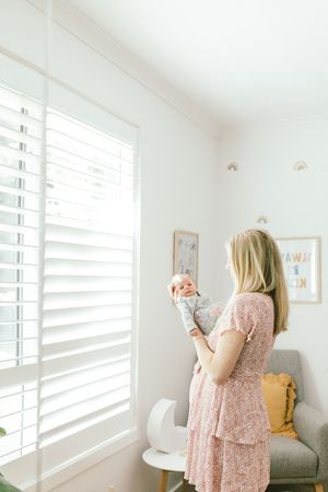 Light filled bedroom interior with white shutters and pink floral dress detail.