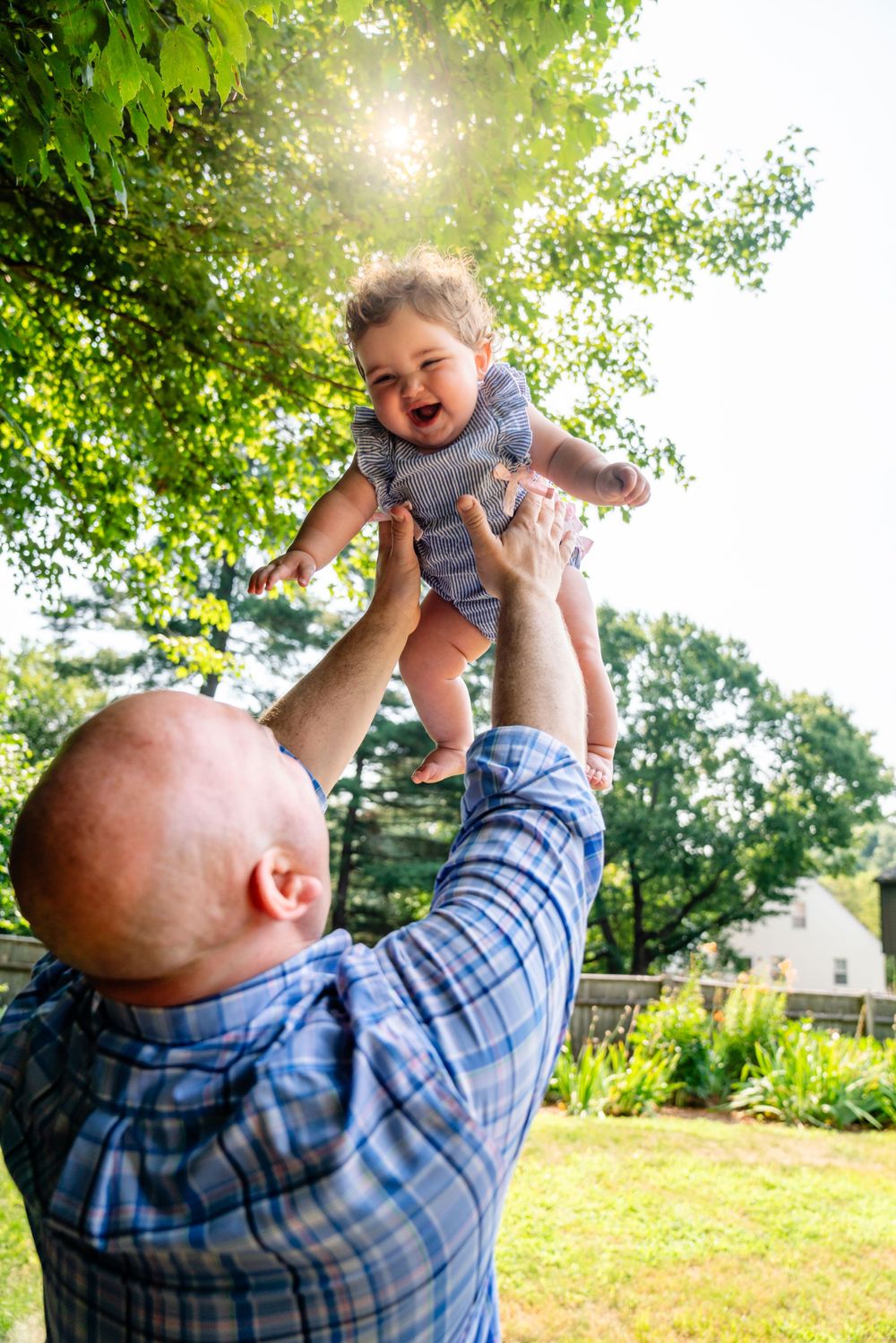 Joyful moment captured as baby is lifted high into air with sunlight streaming through trees.