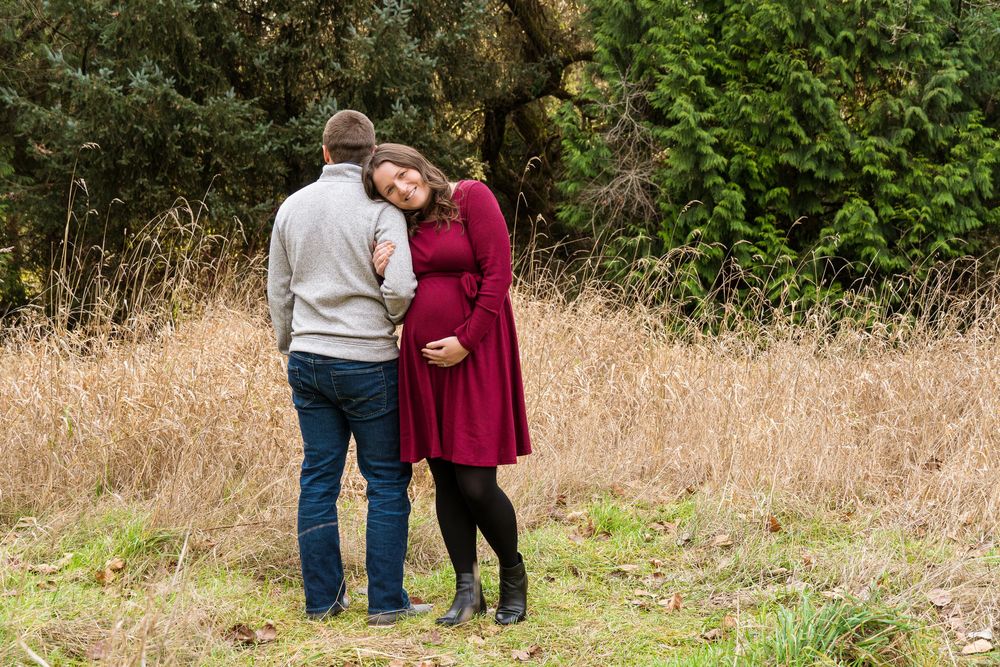 A couple in burgundy and gray attire stands together in a grassy outdoor setting.