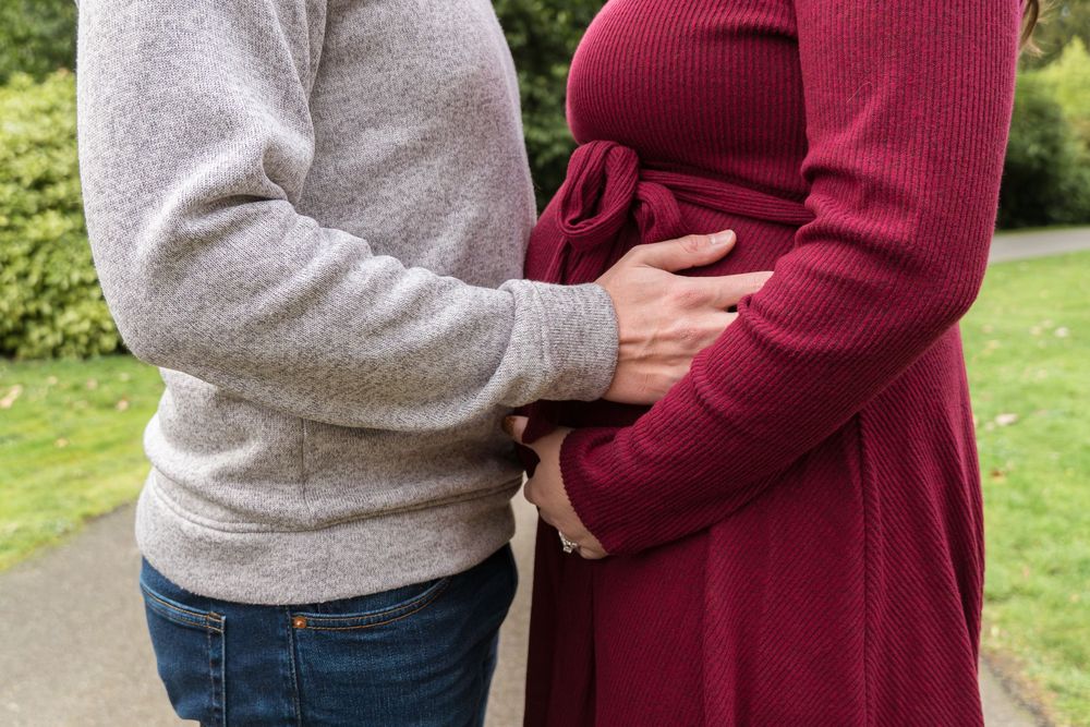 A couple wearing burgundy and gray sweaters holds hands outdoors in a garden setting.