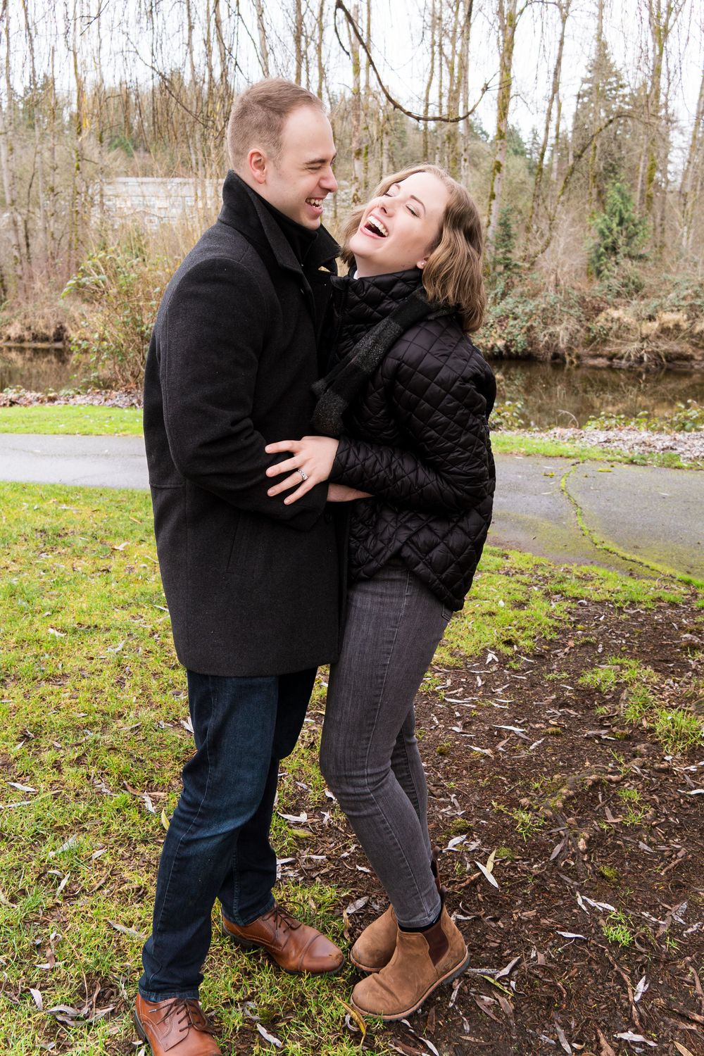 A couple shares a joyful moment together outdoors on a winter day, both wearing dark coats and laughing.