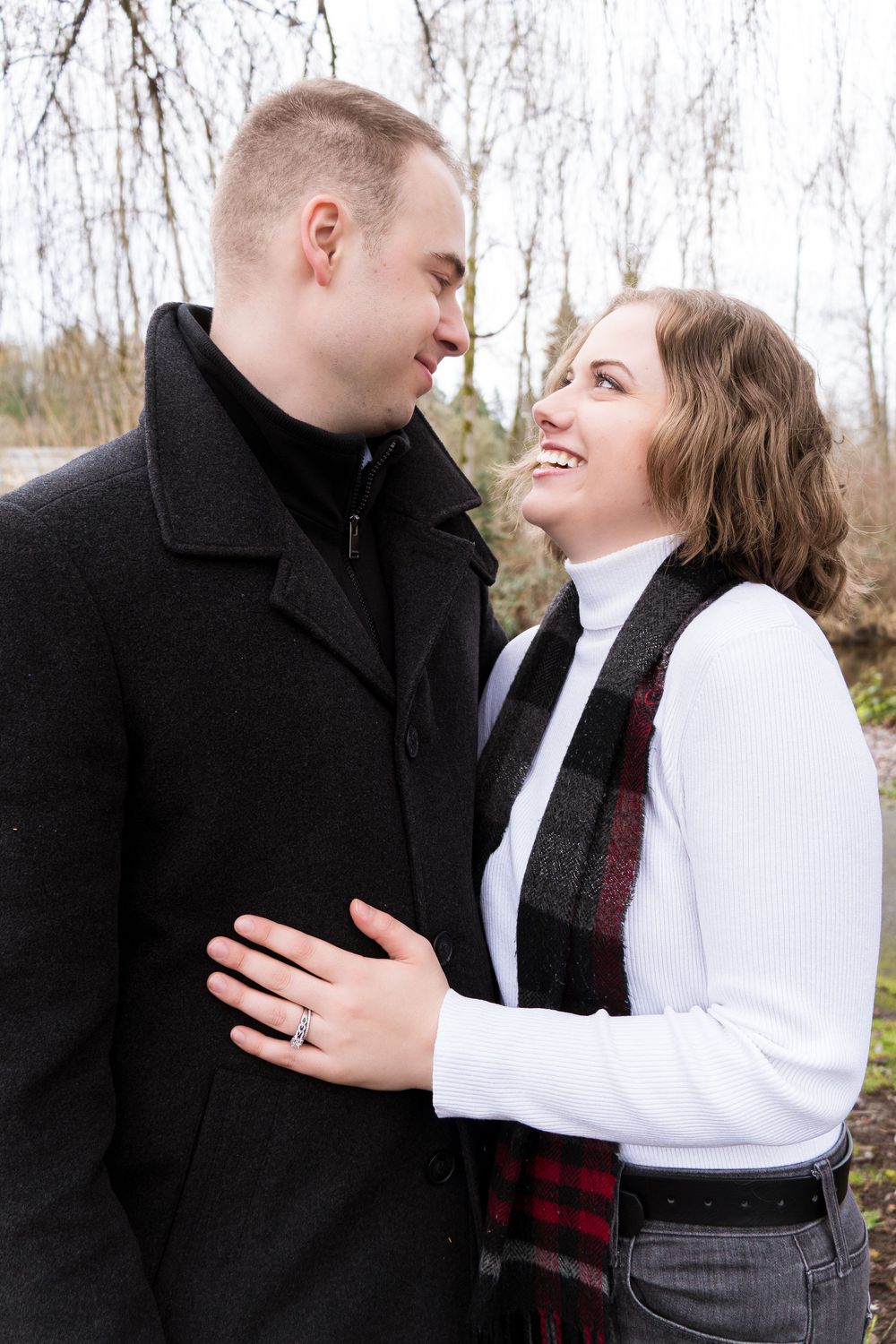 A happy couple shares a loving moment outdoors while wearing winter attire and a plaid scarf.