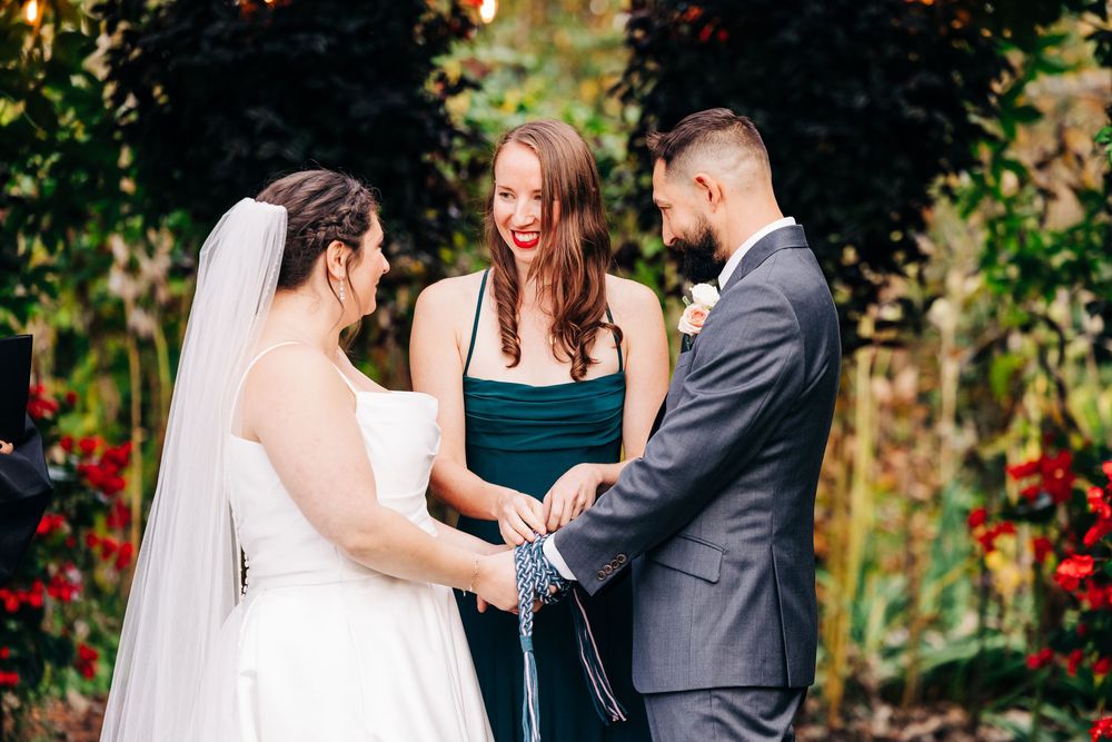 A romantic wedding ceremony takes place in a lush garden setting with vibrant red flowers in the background.