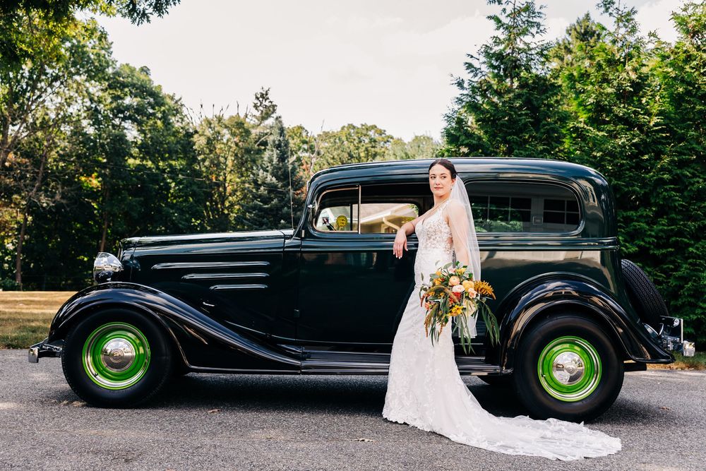 A vintage black 1930s Chevrolet sedan parked outdoors with bright green wheels serves as an elegant wedding photo backdrop.