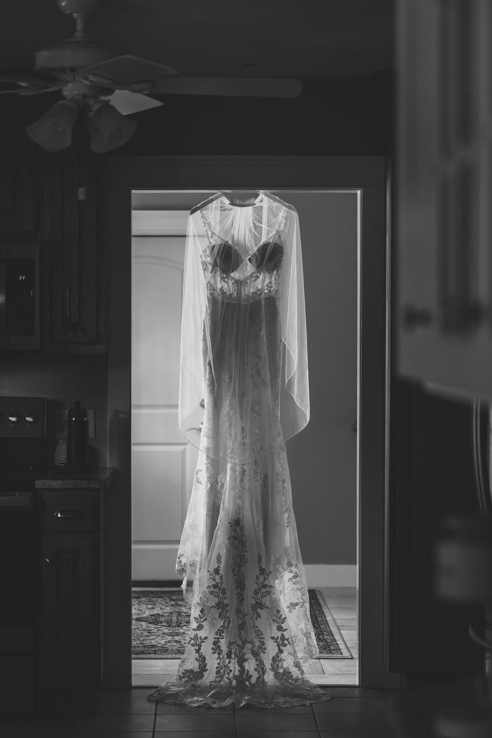 A vintage white lace wedding dress displayed in a dark room with dramatic backlighting creating an ethereal glow.