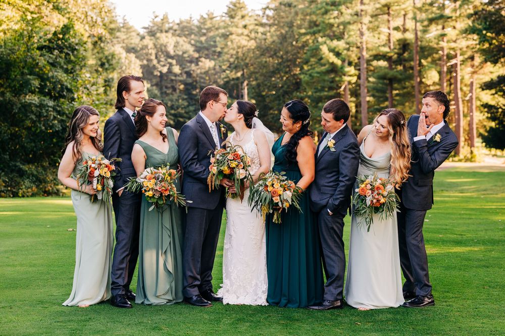 Wedding party poses together on a lush green lawn during golden hour sunset at an outdoor ceremony.