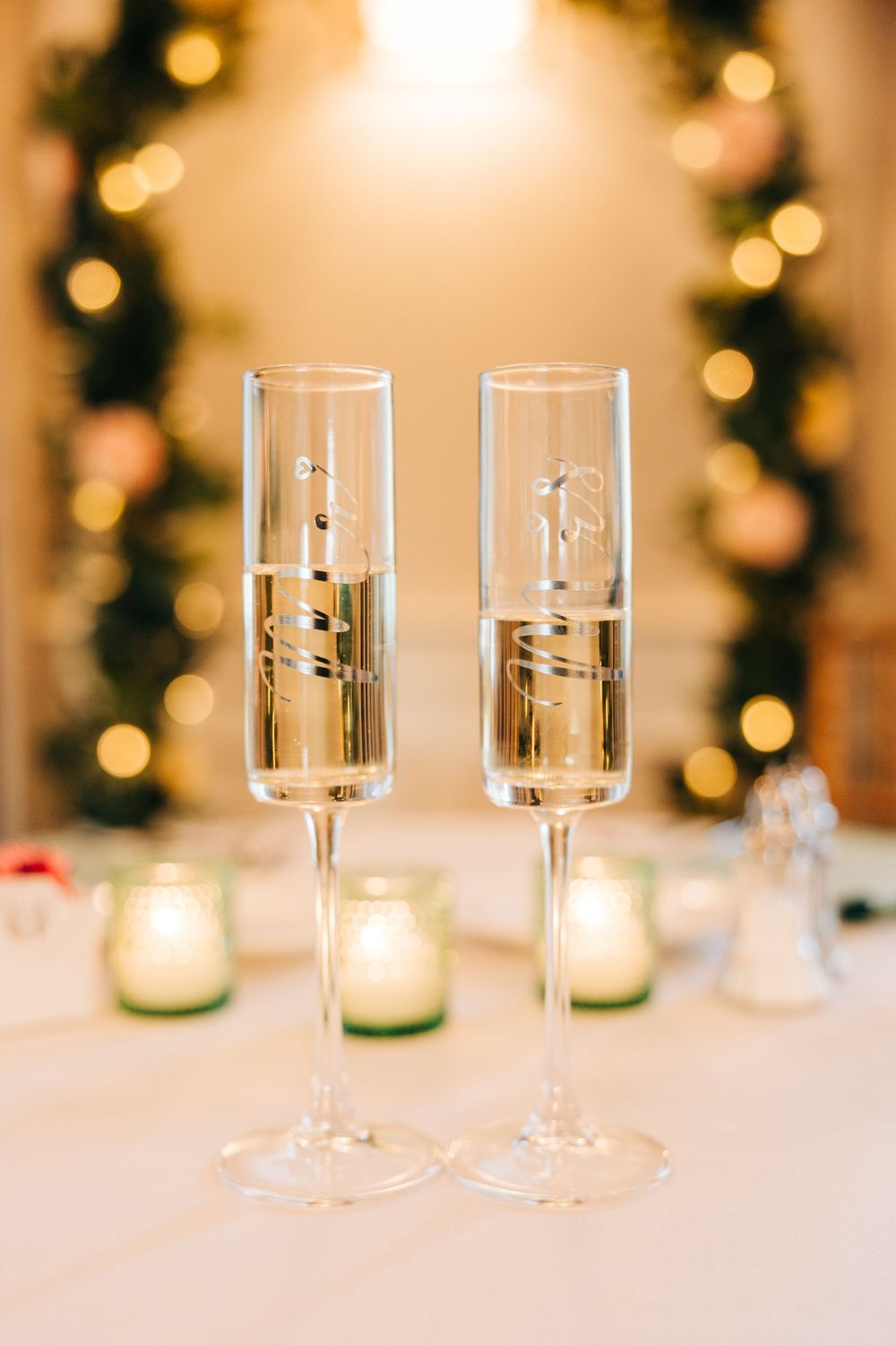Elegant champagne glasses with soft bokeh lights and blurred Christmas decorations in the background create a festive atmosphere.