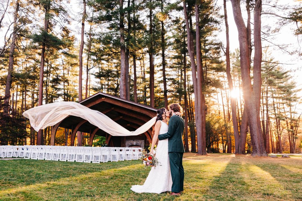 Couple celebrates at sunset outdoor wedding ceremony in pine forest with veil flowing in golden light.