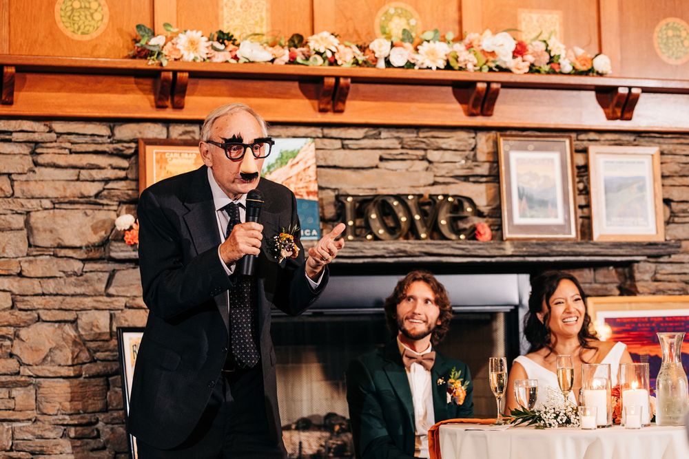 Wedding reception guests enjoying speeches and toasts in a rustic stone-walled venue with mood lighting.