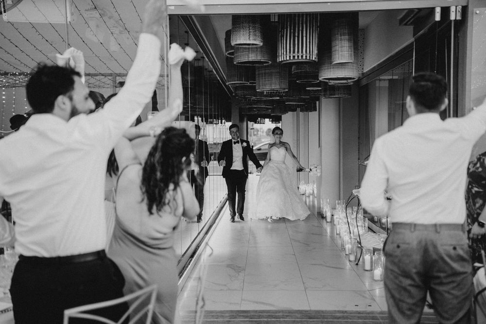 Wedding guests cheer and celebrate as a couple makes their entrance down an industrial-style venue hallway in black and white.