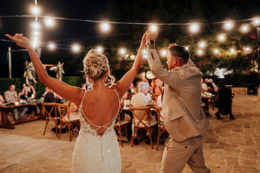 Couples dance and celebrate under twinkling string lights at an outdoor evening wedding reception.
