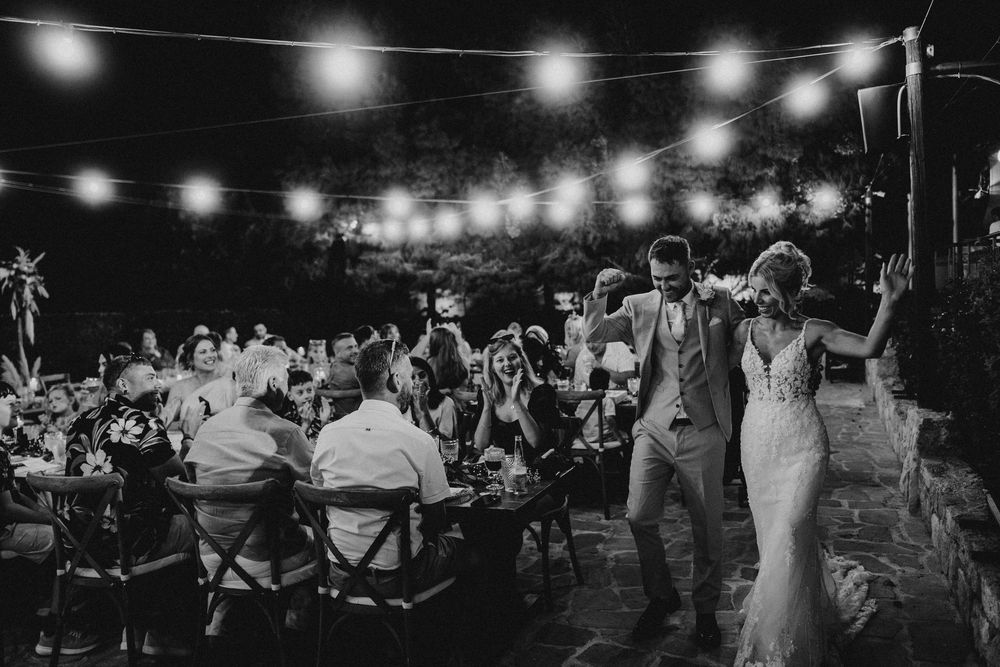 Black and white photo of an outdoor wedding reception at night with string lights illuminating guests dancing and celebrating.