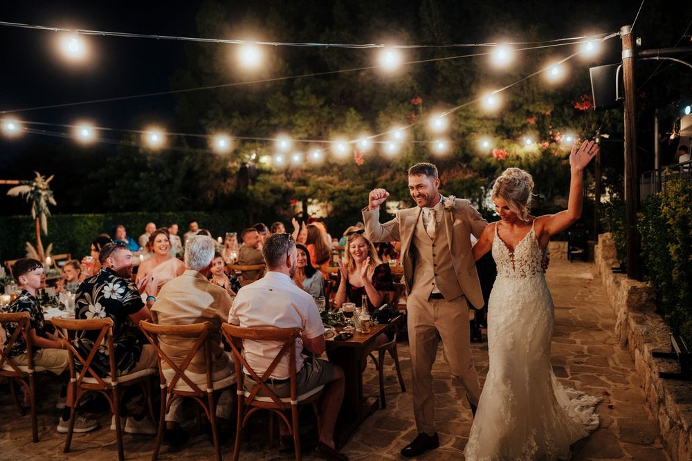 String lights illuminate an outdoor evening wedding reception with wooden tables and chairs arranged under the night sky.