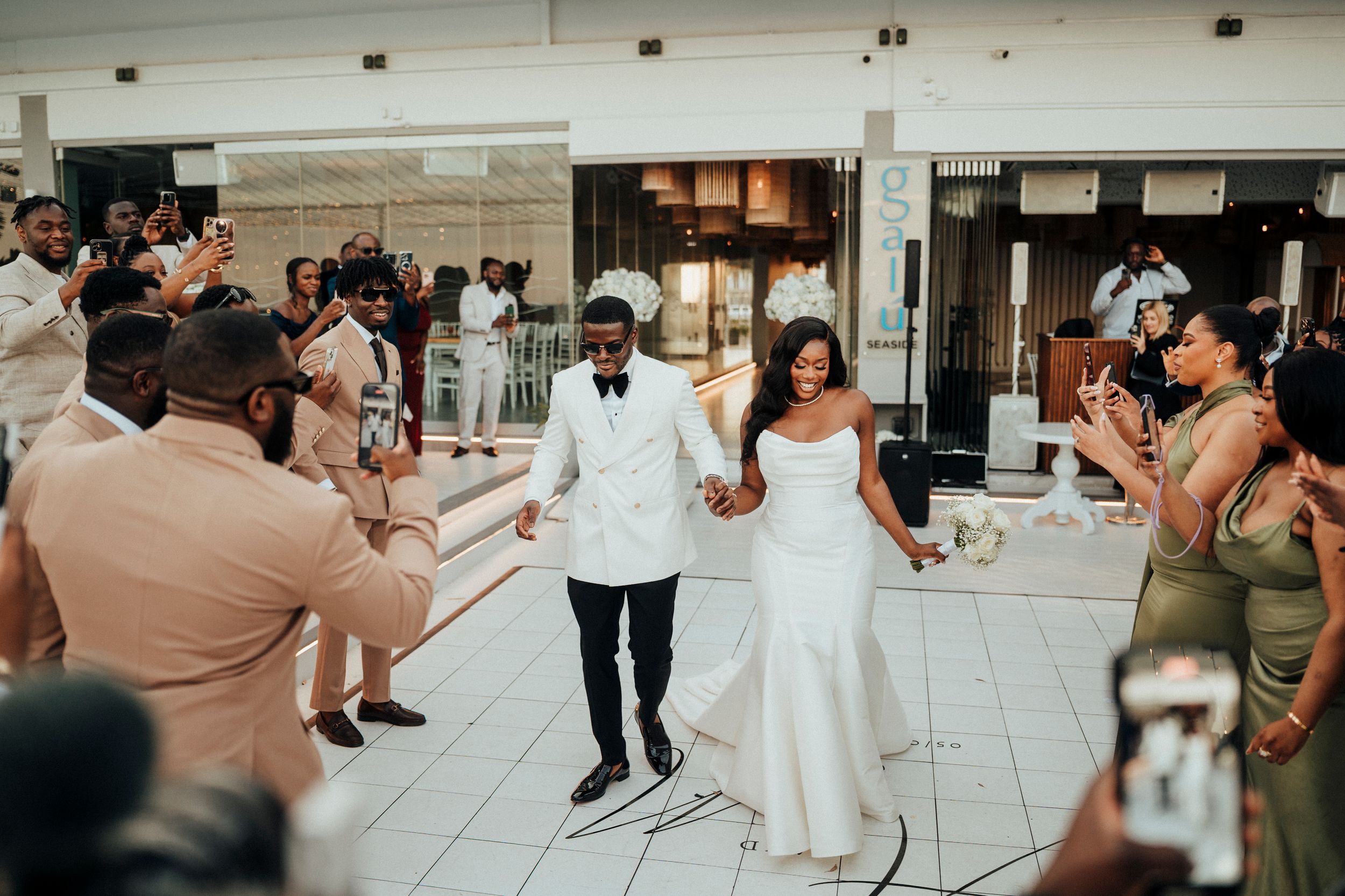 Wedding guests dance and celebrate together on a tiled dance floor at an indoor reception venue.