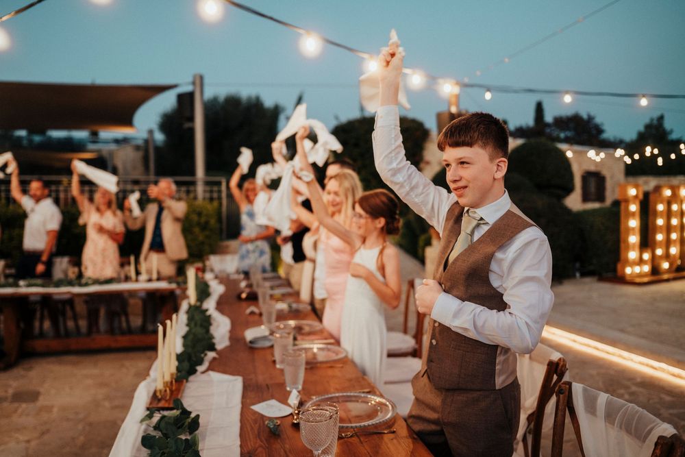 String lights illuminate an outdoor wedding reception dance floor as guests celebrate and dance at dusk.