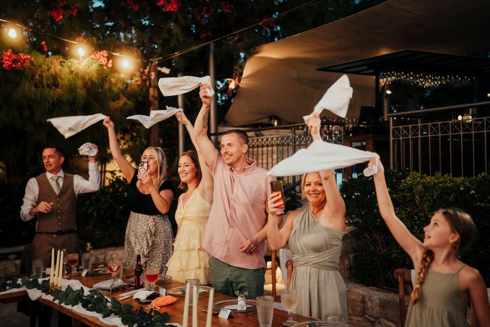 Wedding guests dance and celebrate at an outdoor evening reception under string lights and white canopy tents.