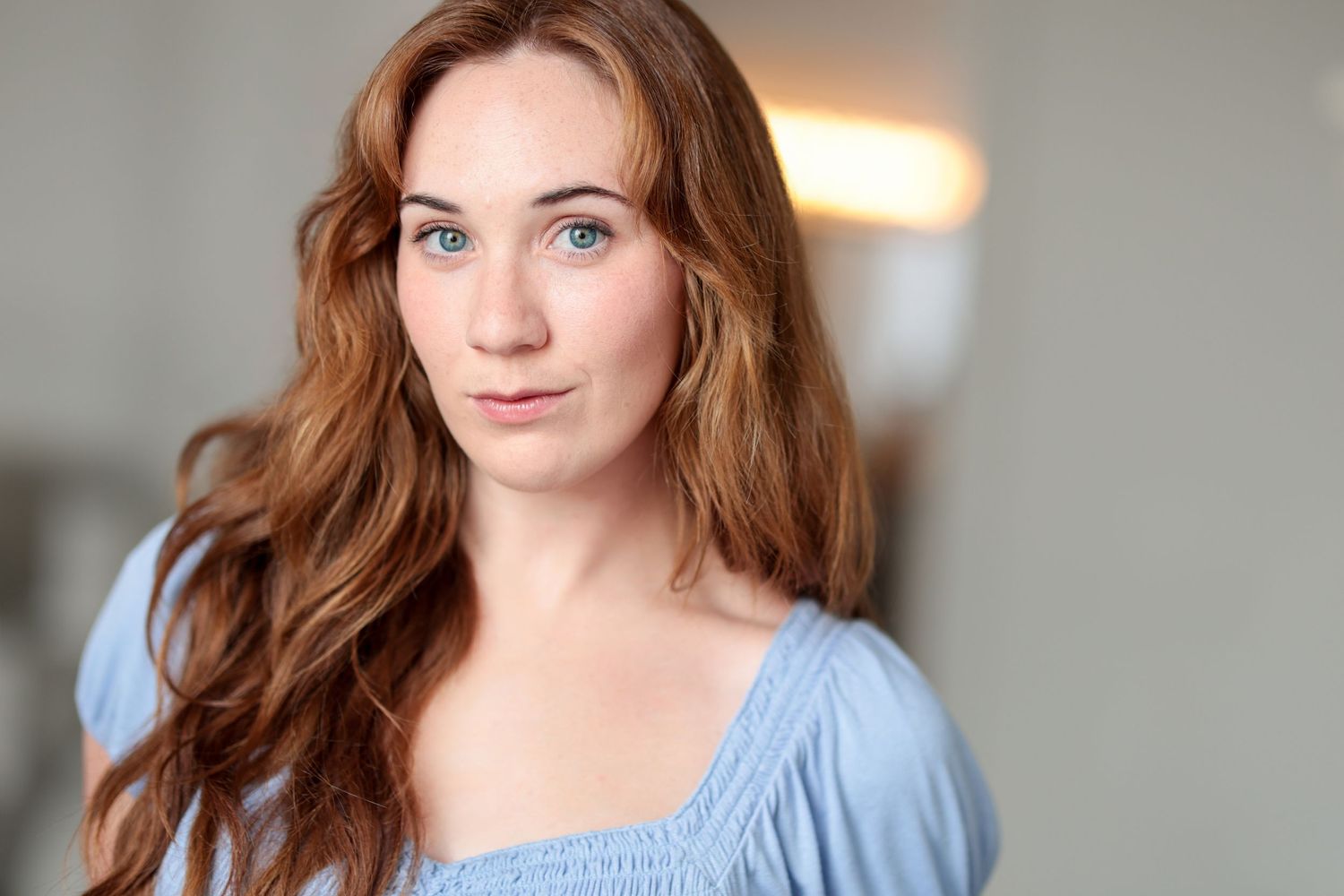 Portrait of woman in light blue dress with soft window lighting.
