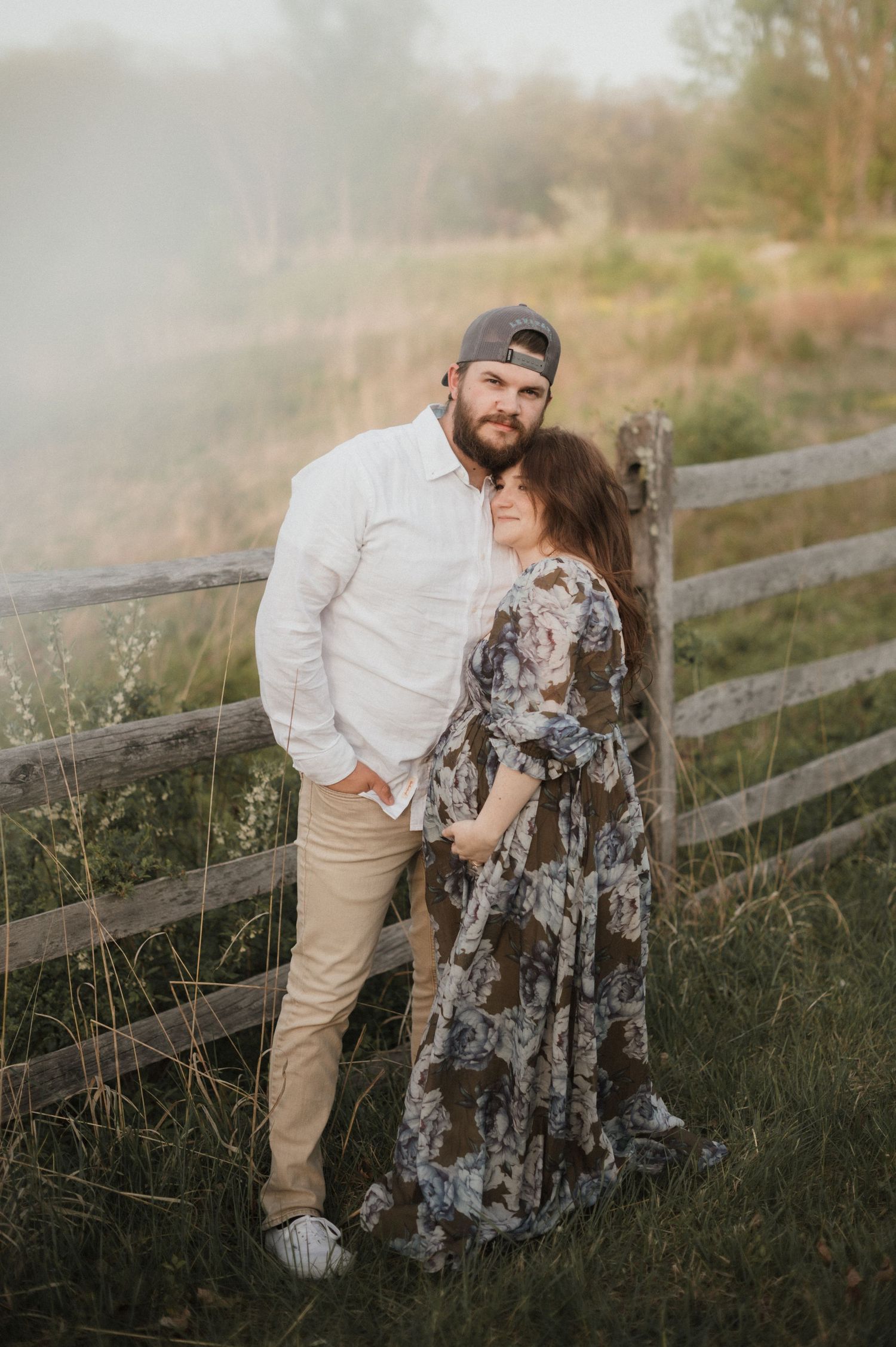 A couple posing against a rustic wooden fence in casual and dressy attire.