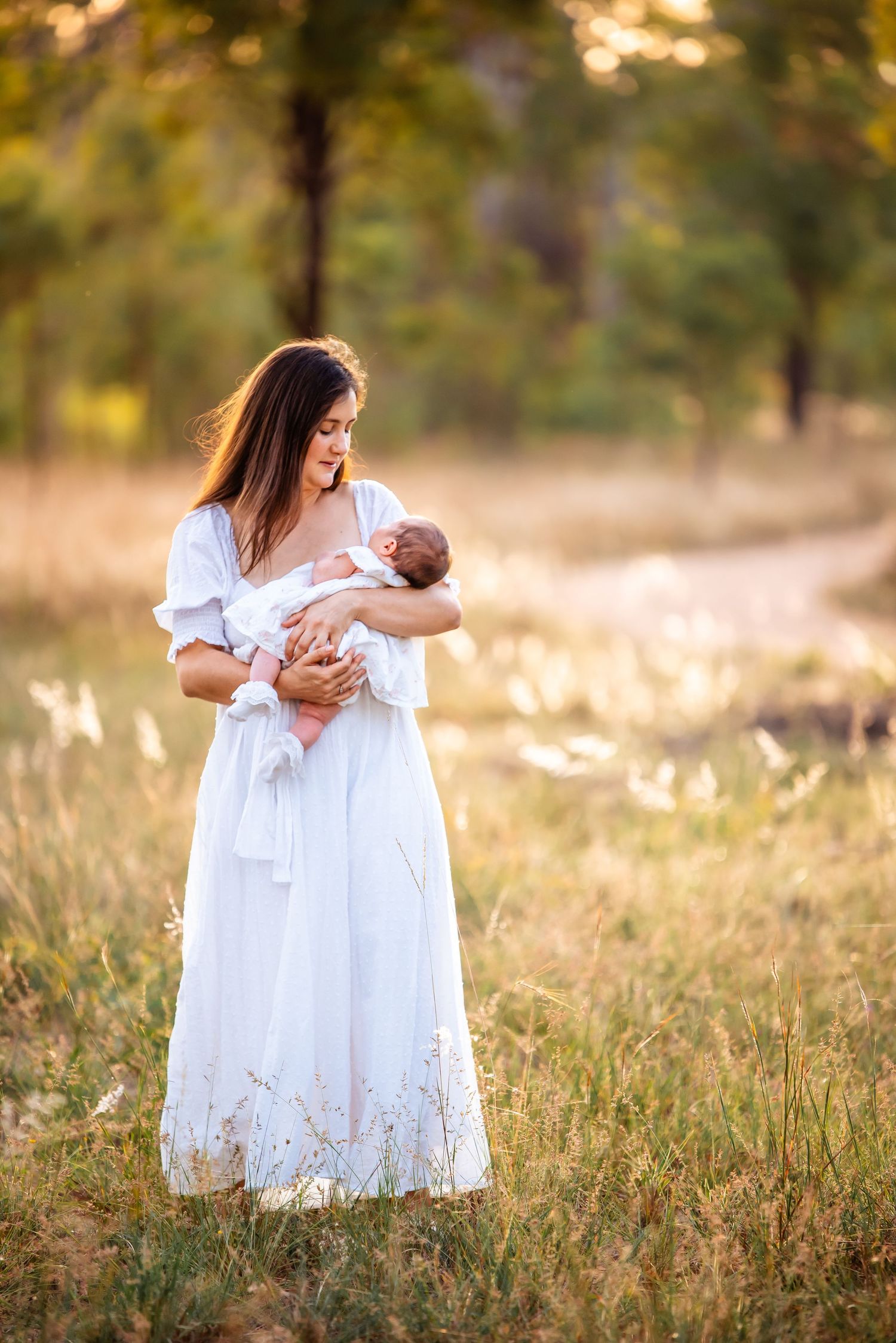 A tender moment between mother and newborn in a white dress at sunset.