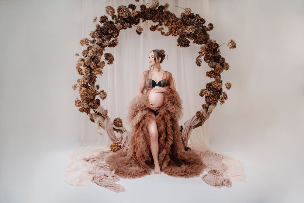 A romantic maternity photo featuring a floral arch backdrop and flowing dusty rose fabric draping  Babybauch Fotografie Hessen