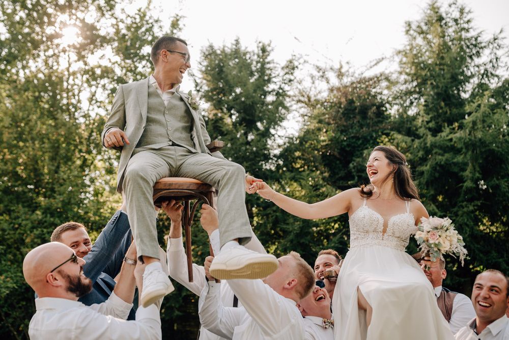 Wedding party celebrates outdoors with traditional chair lift during sunset ceremony in garden setting. Hochzeit Burg Ronneburg