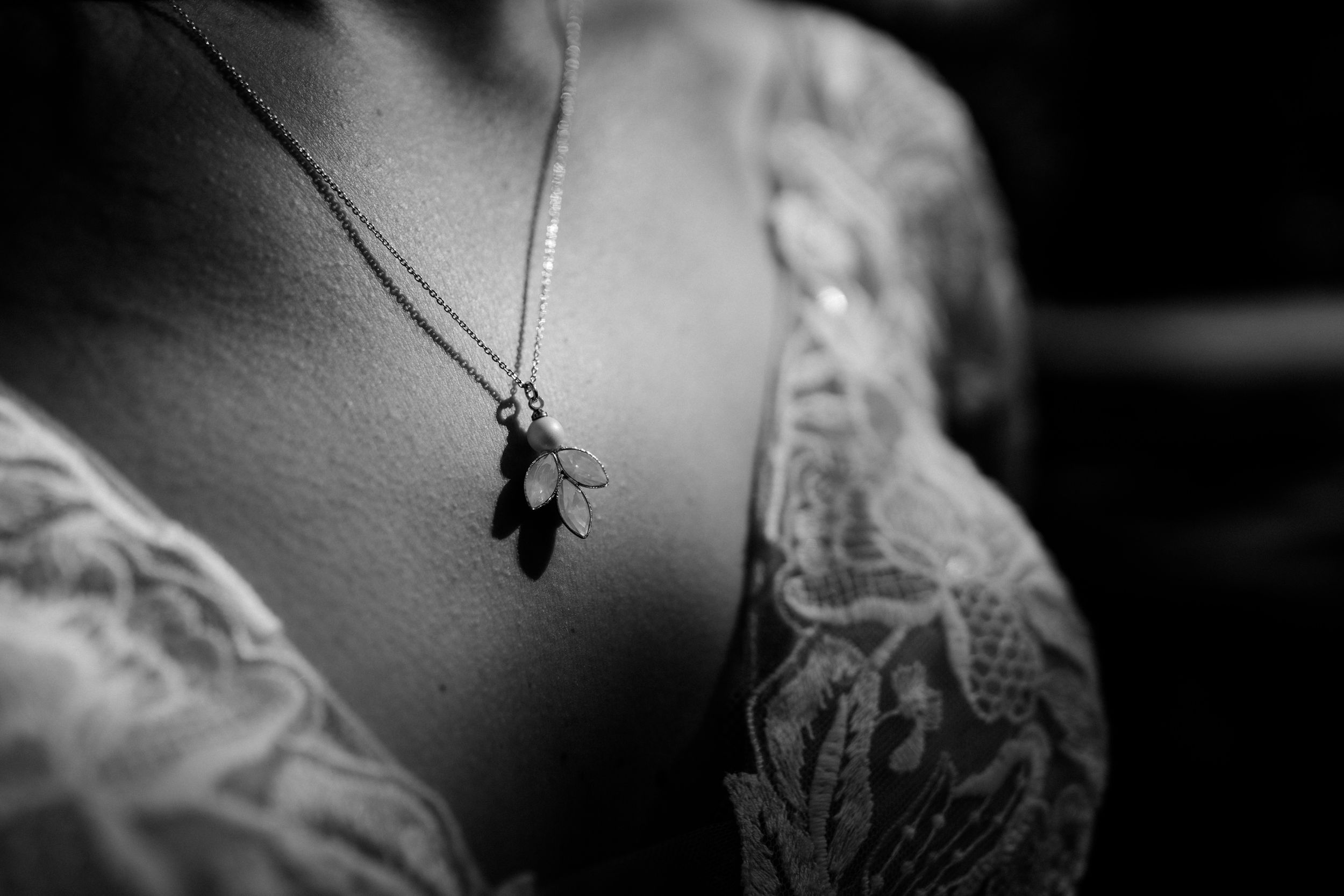 Close-up detail shot of delicate necklace against lace wedding dress.
