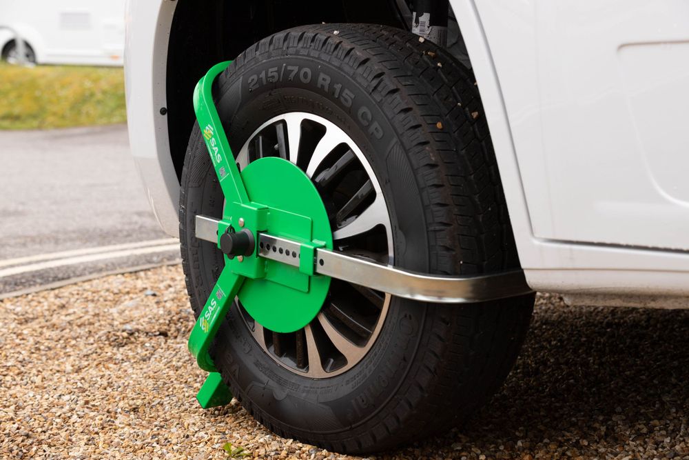 Bright green wheel clamp security device attached to a white vehicle's tire.