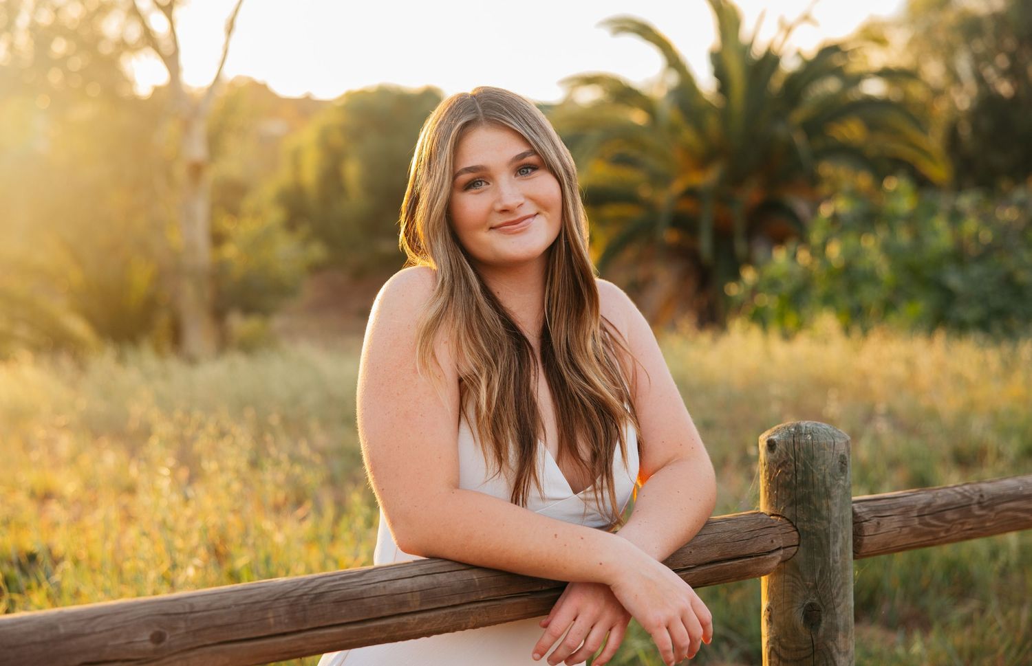 Person leaning on wooden fence post during golden hour in rural setting.