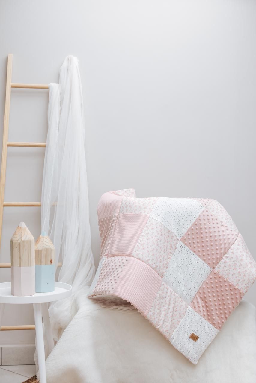 Soft pink and white patchwork quilt displayed with decorative wooden ladder and sheer curtains.