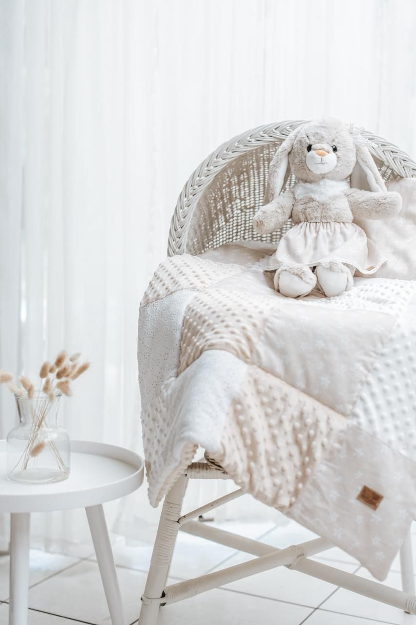 White plush minky blanket and stuffed bunny toy arranged on white rocking chair in cozy nursery setting.