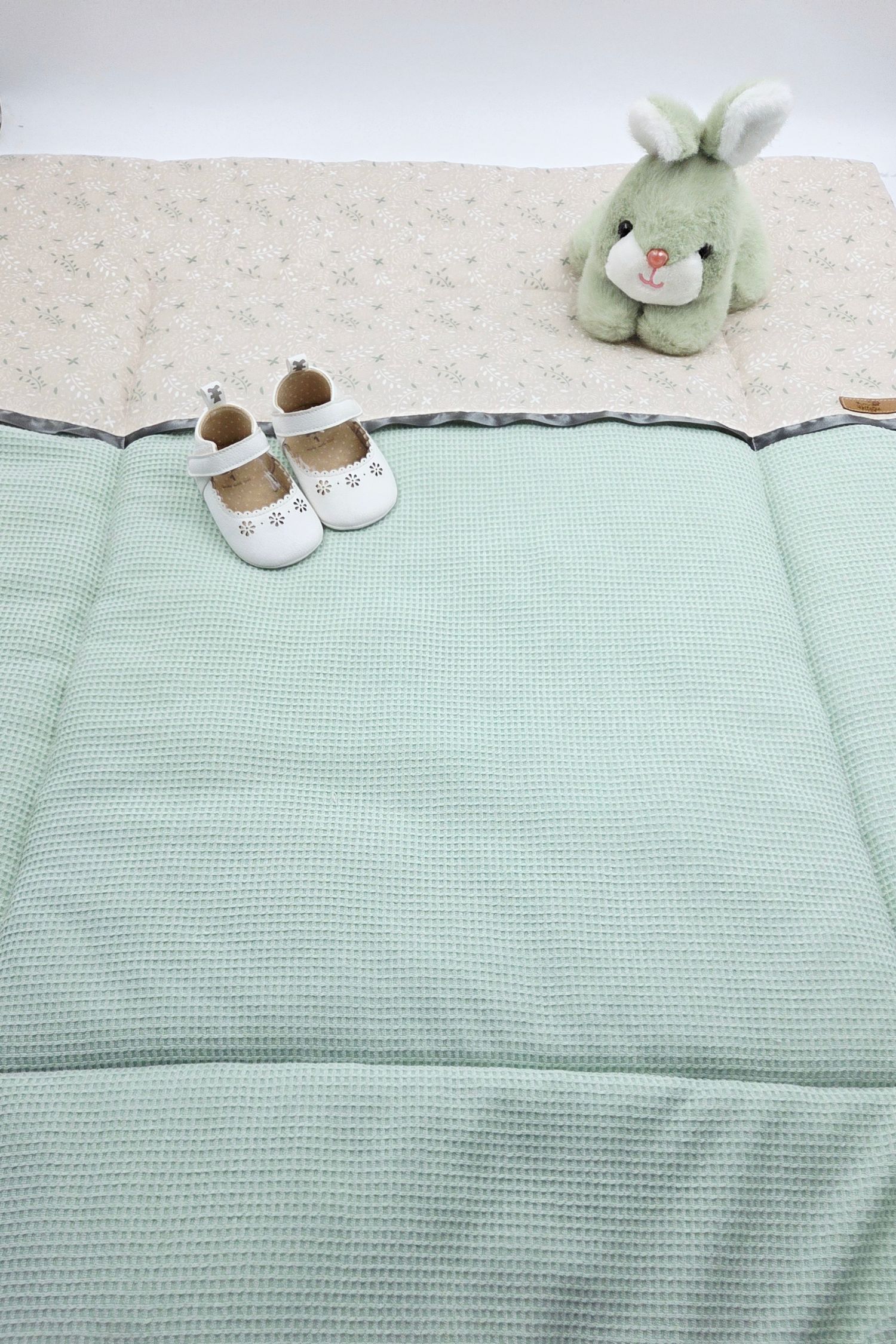 Mint green waffle blanket with white baby shoes and plush bunny.