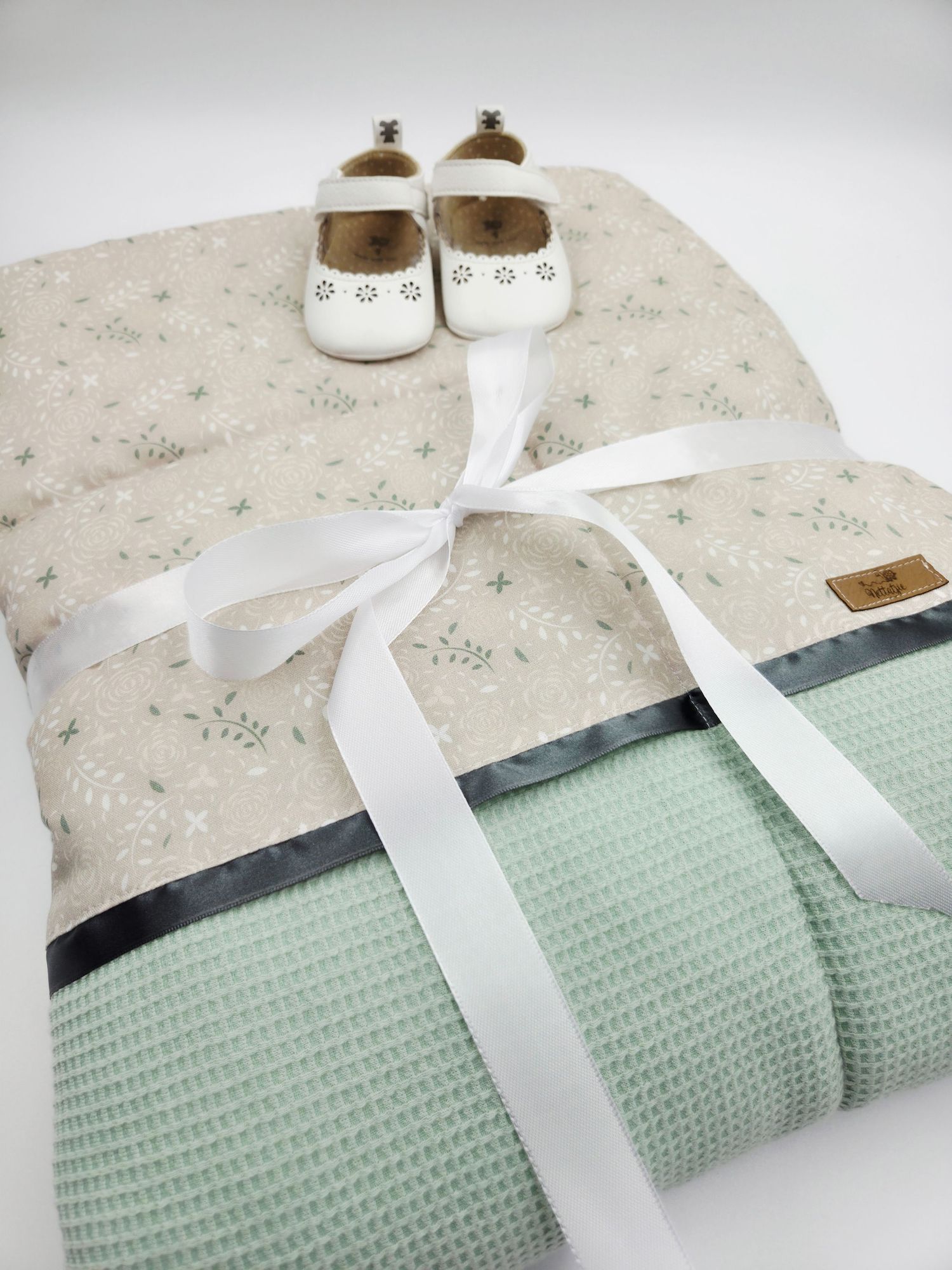 Mint green waffle blanket with white satin bow and baby shoes on display.