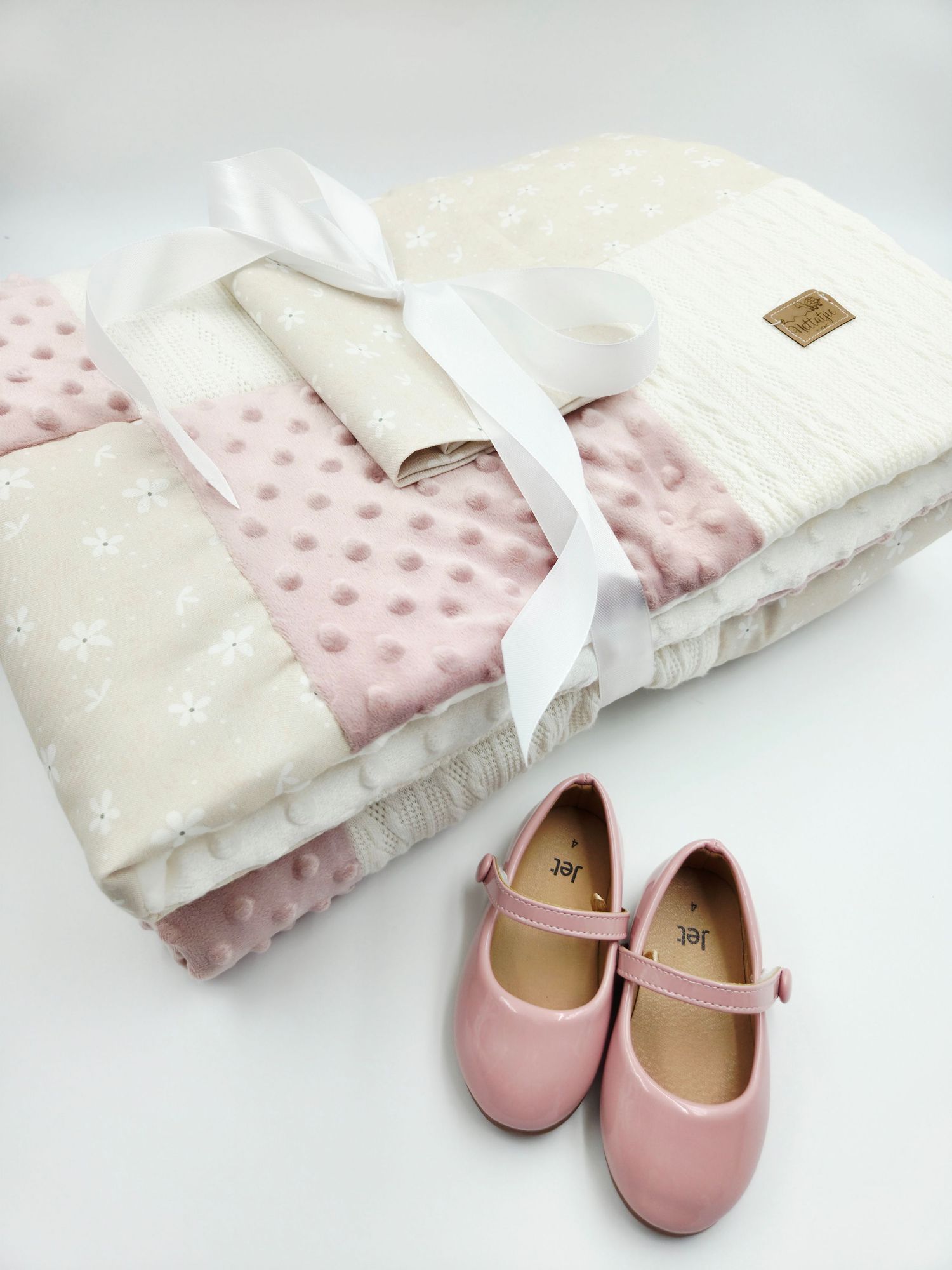 Pink and white baby blanket with matching pink shoes arranged in a delicate display.