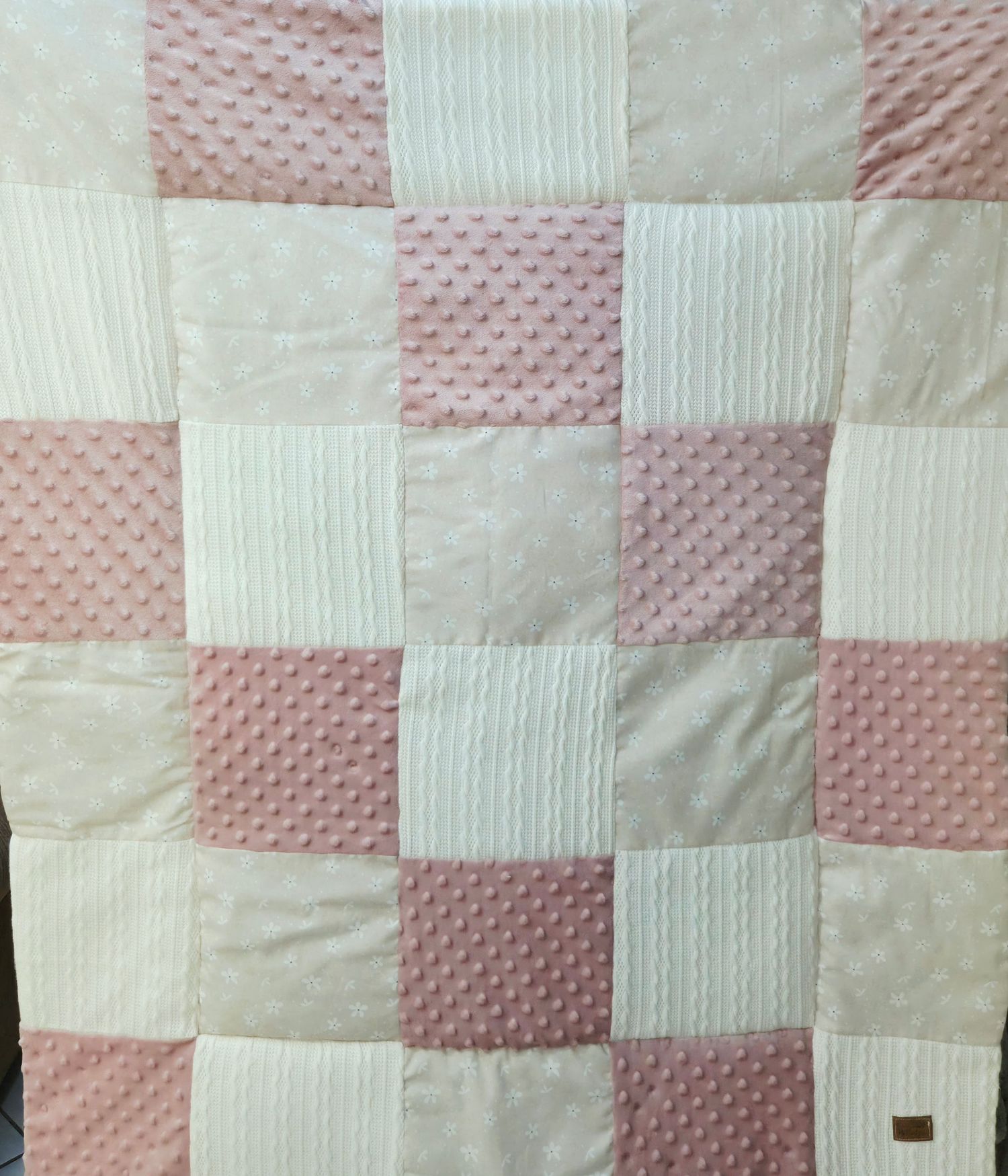 Patchwork baby blanket in soft pink and white squares with textured patterns.