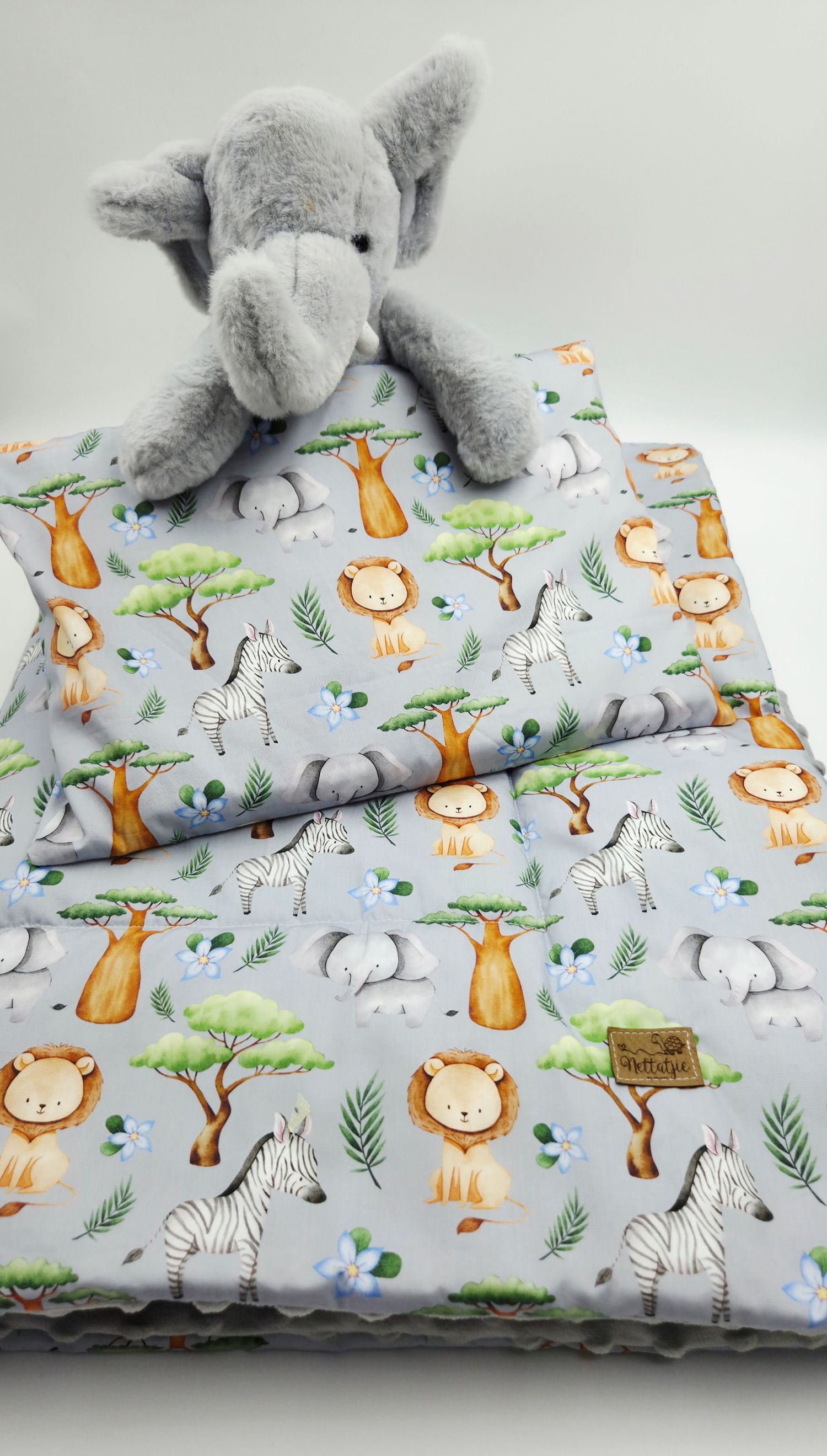 Safari-themed baby blanket with lions, zebras, and trees on light gray background.