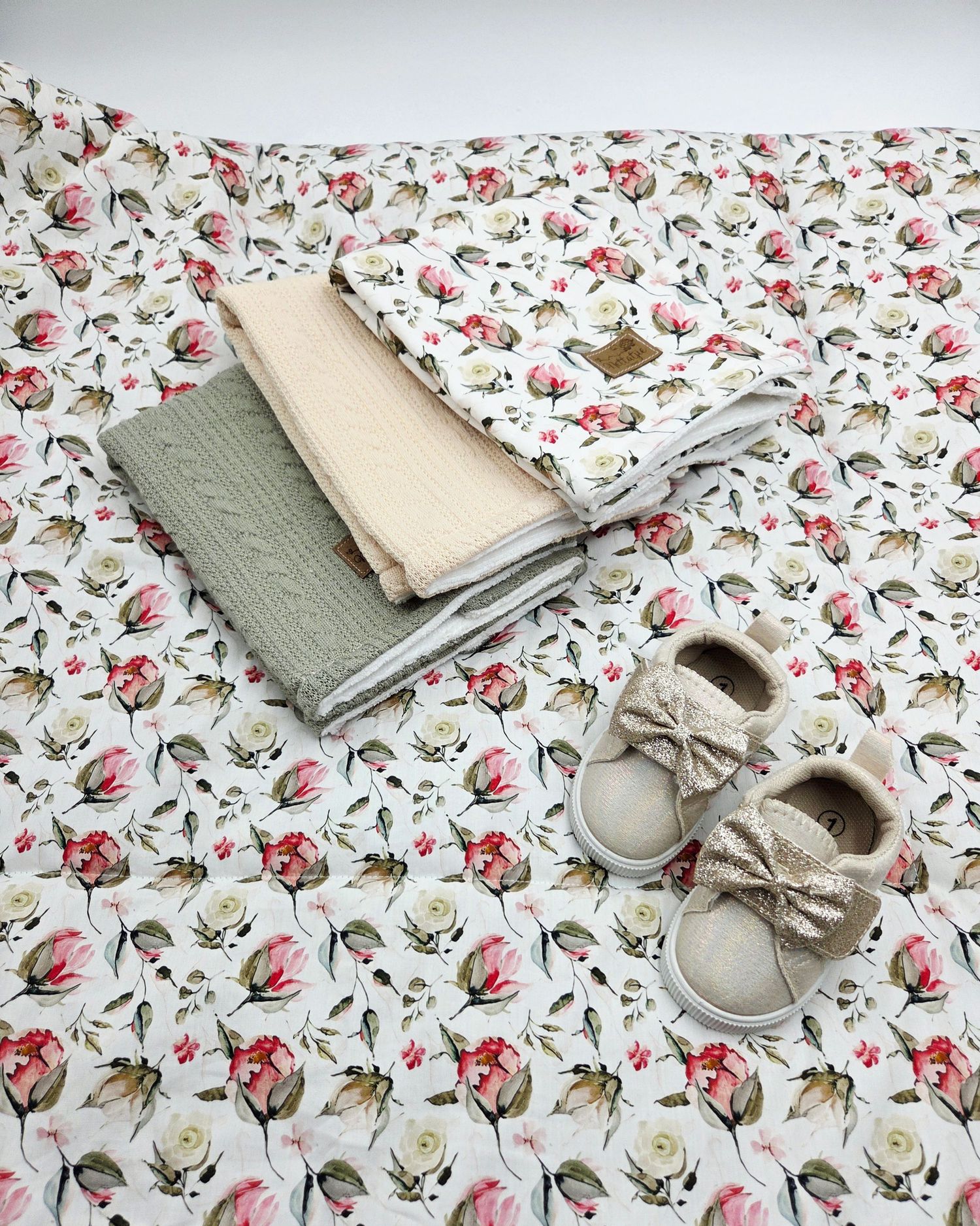 Floral print baby blanket with gray accessories and delicate shoes.