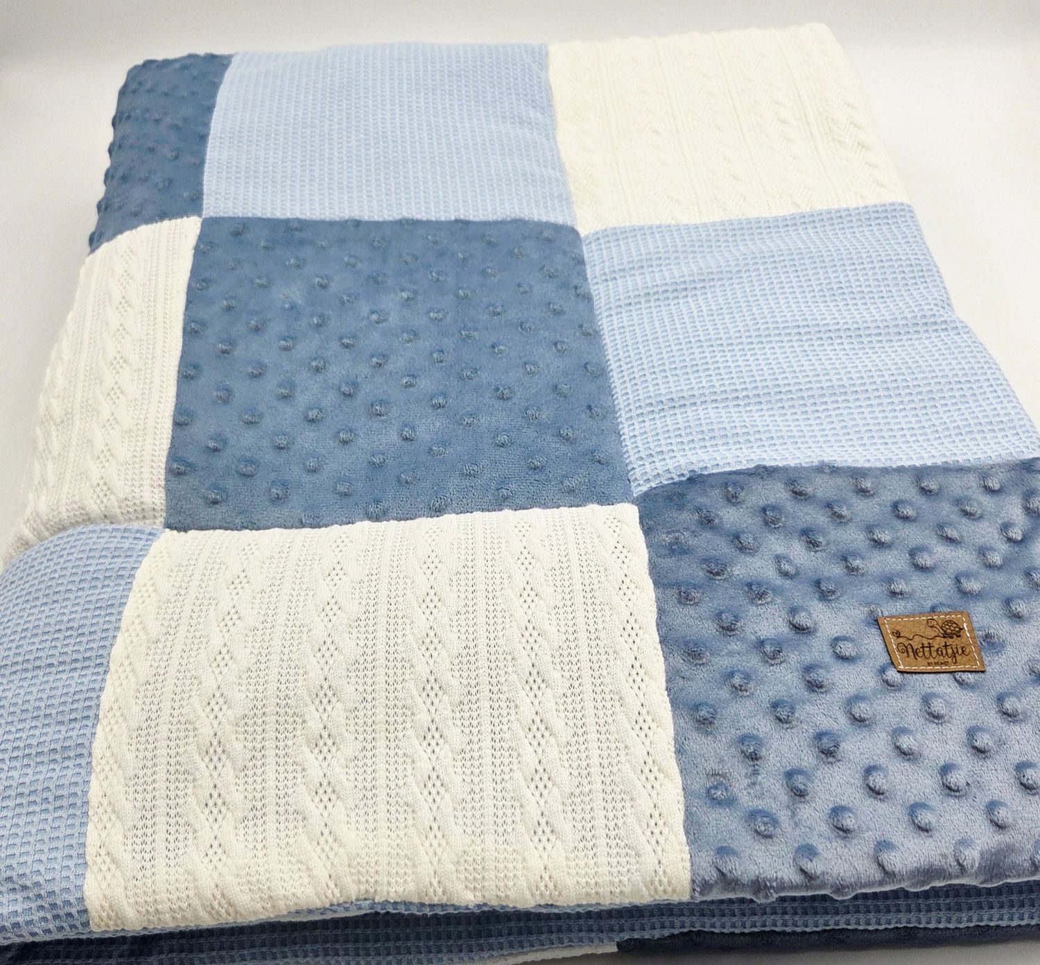 Patchwork baby blanket in blue and white with cable knit and minky dot textures.