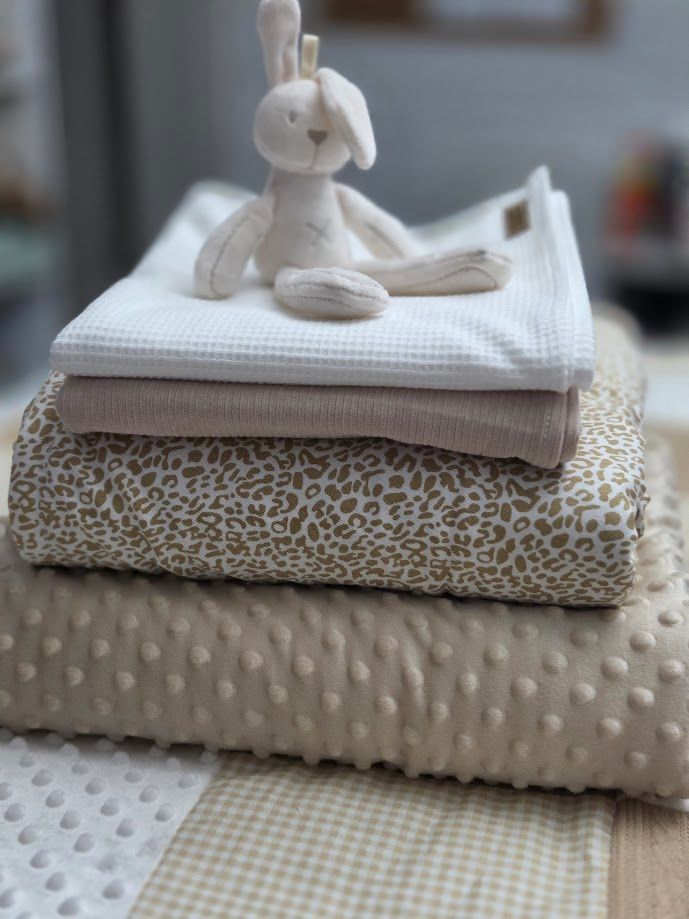 Stack of neutral baby blankets in cream and gold leopard print, topped with a white plush bunny toy.