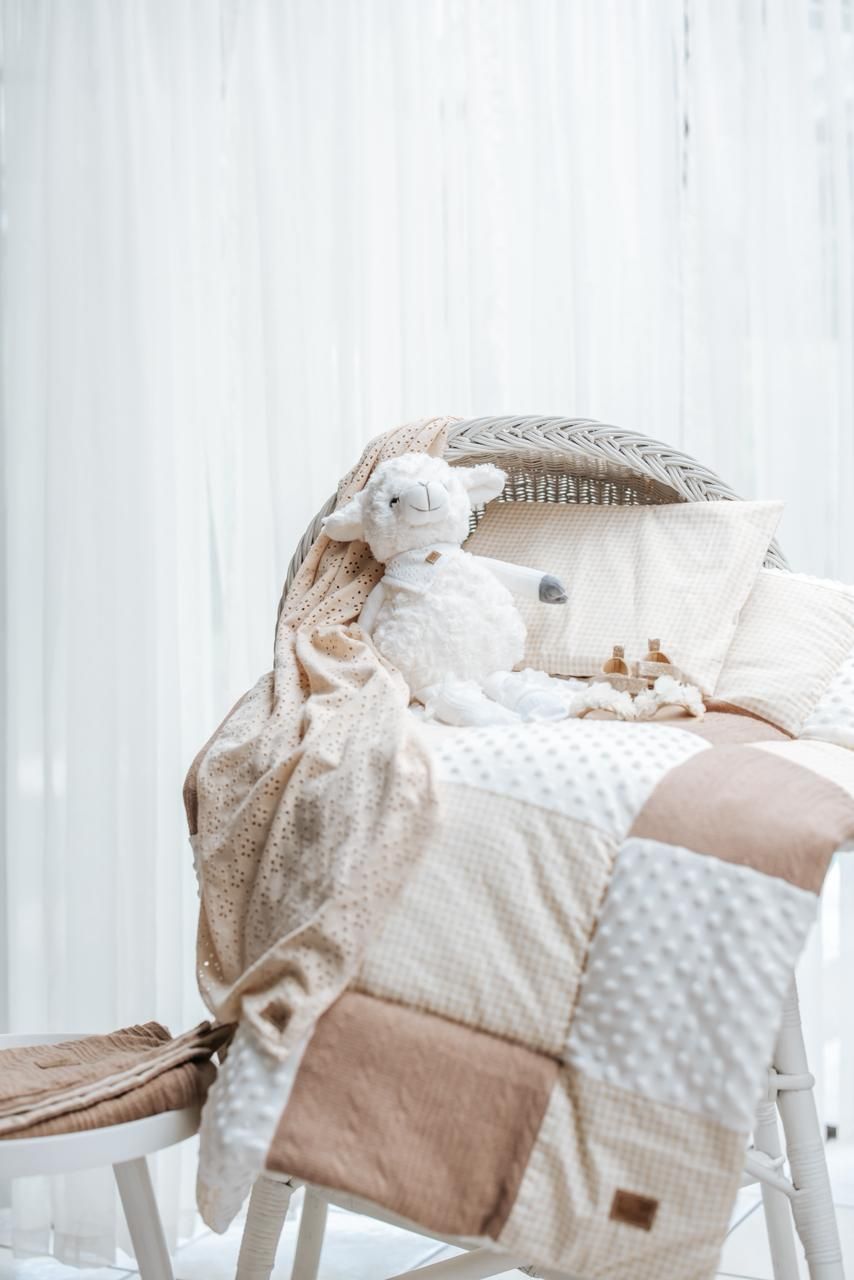 Neutral-toned baby bedding and blankets with delicate patterns arranged in a cozy nursery setting.