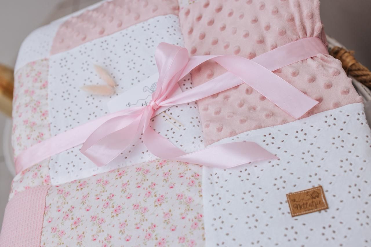 Pink and white baby blanket with delicate floral patterns and ribbon details.