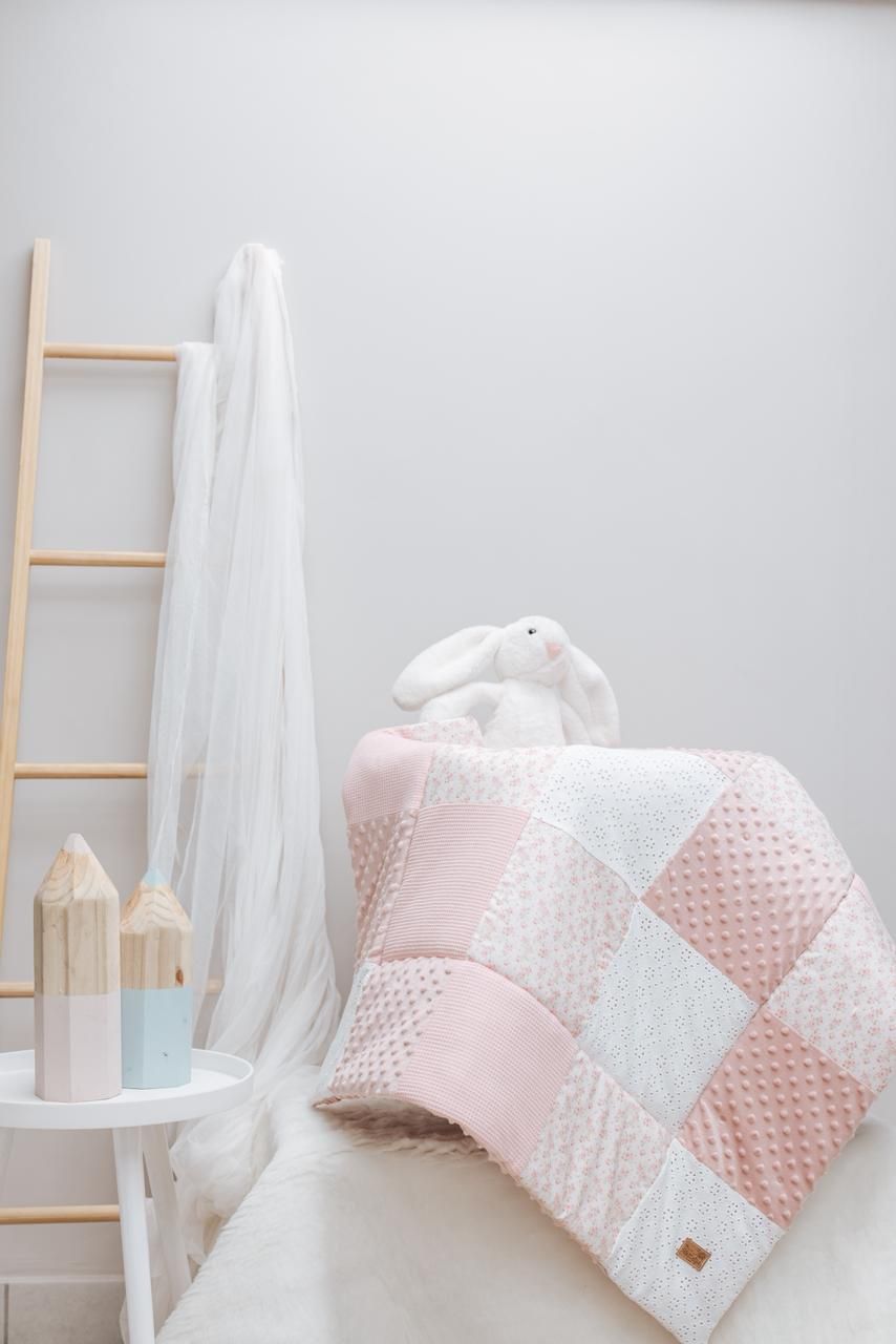 Nursery decor featuring pink textured blanket with white accents and wooden ladder.
