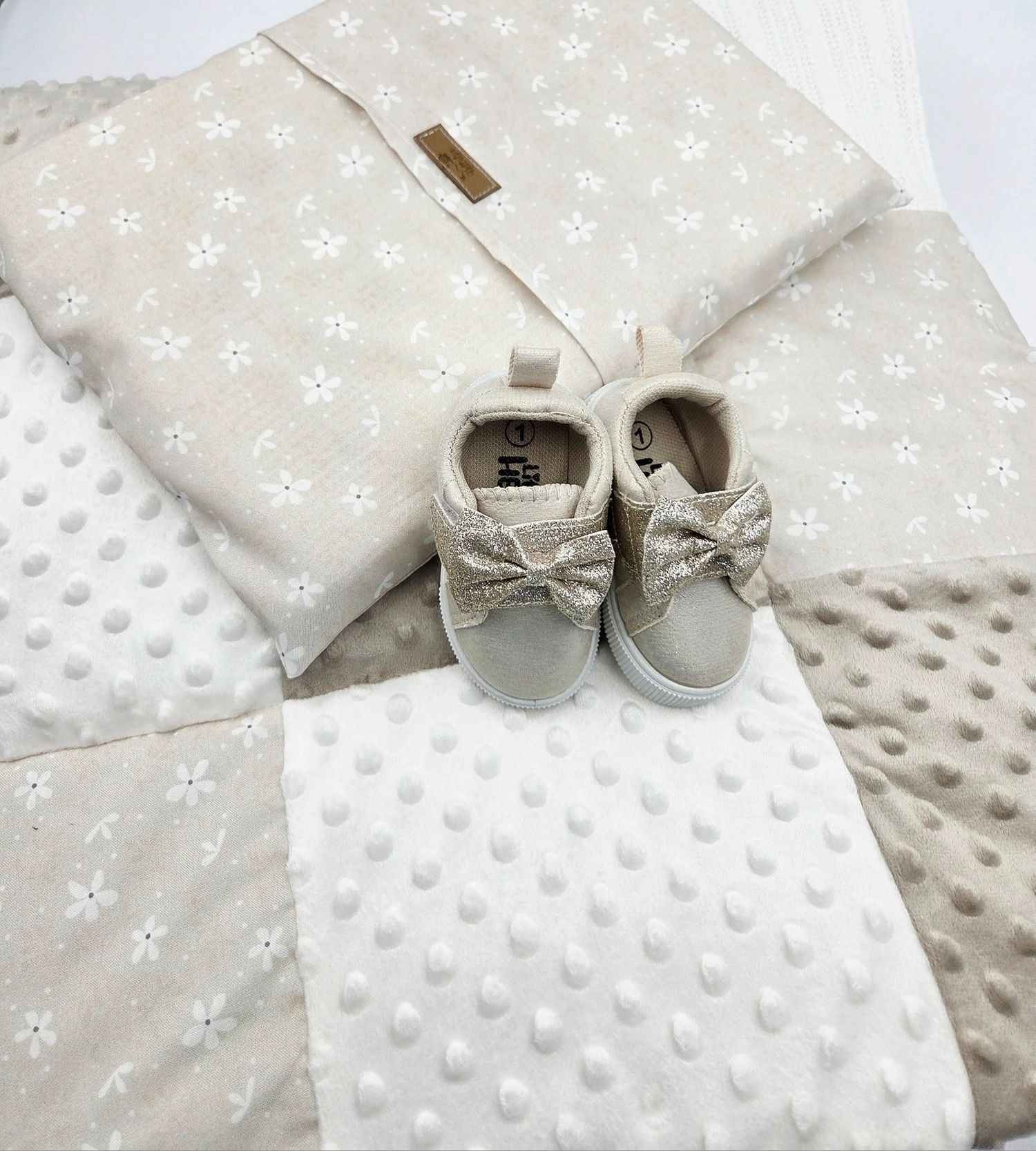 Neutral colored baby blanket with white ribbon and gray bow shoes accent.