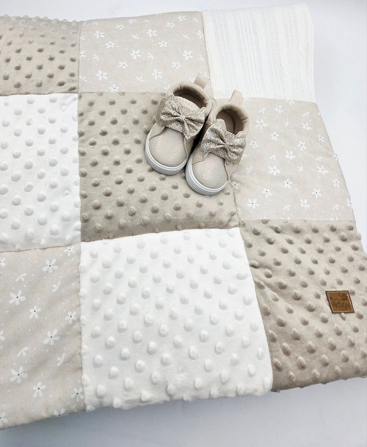 Neutral toned baby blanket featuring bow-adorned shoes and textured fabric design.