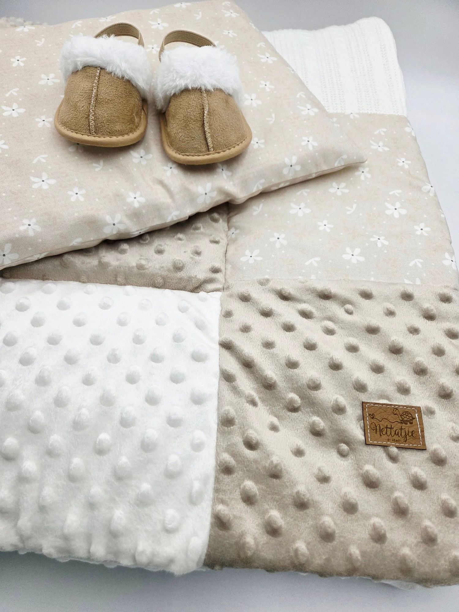 Plush baby blanket in beige and white with minky dot texture and leather tag detail.