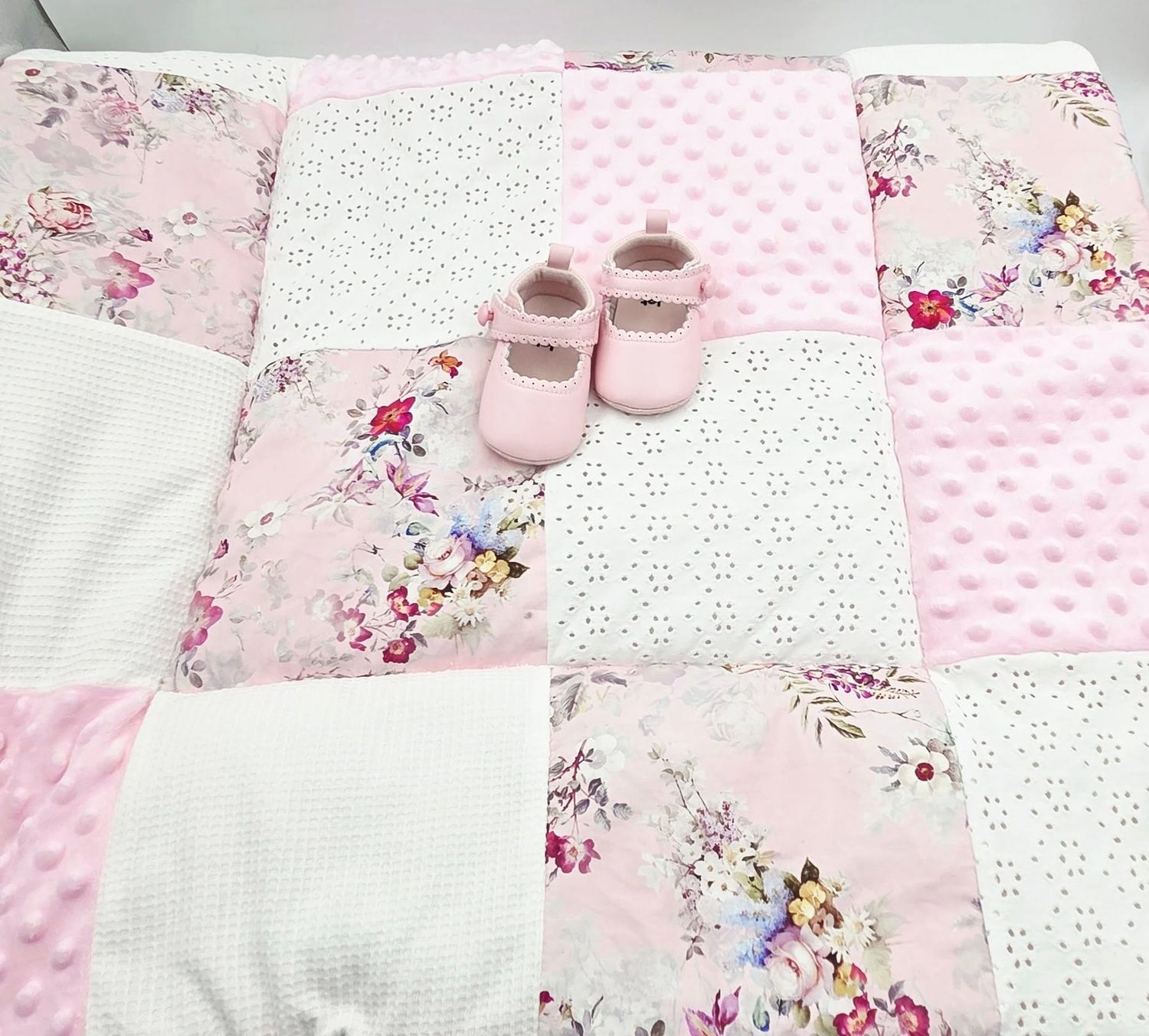 Pink floral baby blanket with delicate pattern and matching shoes accent.