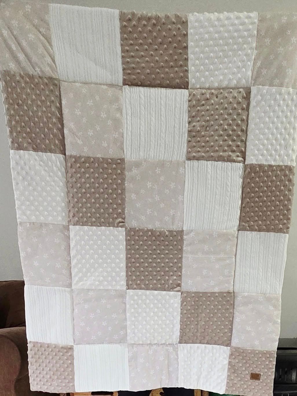 Patchwork quilt pattern in neutral beige and white tones with textured squares.